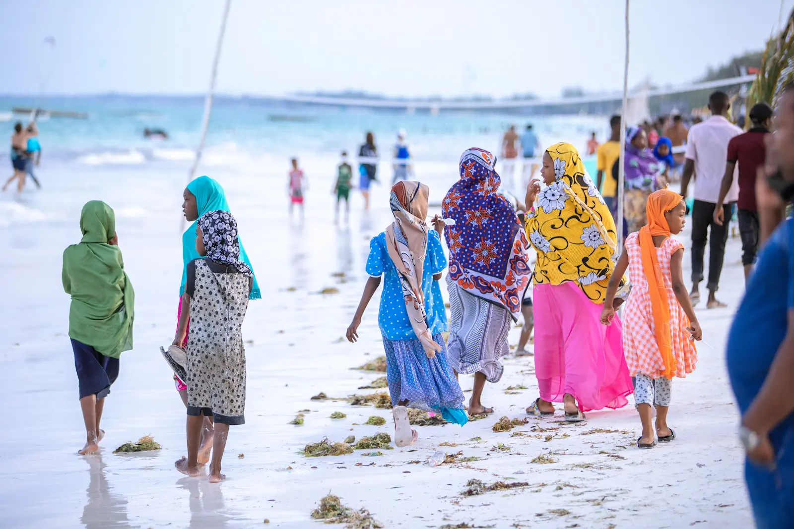 Women and children in colourful traditional dress walking along a Zanzibar beach