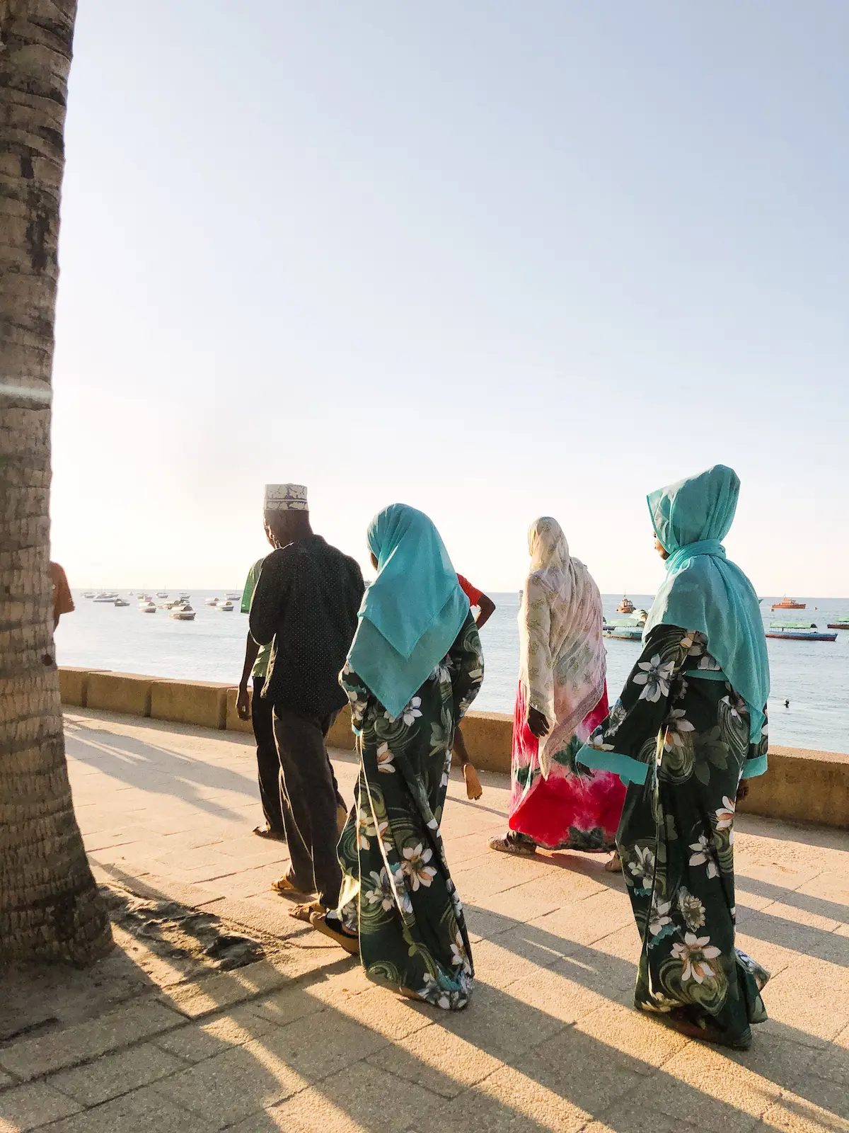 Locals in traditional dress walking along the Stone Town waterfront at sunset