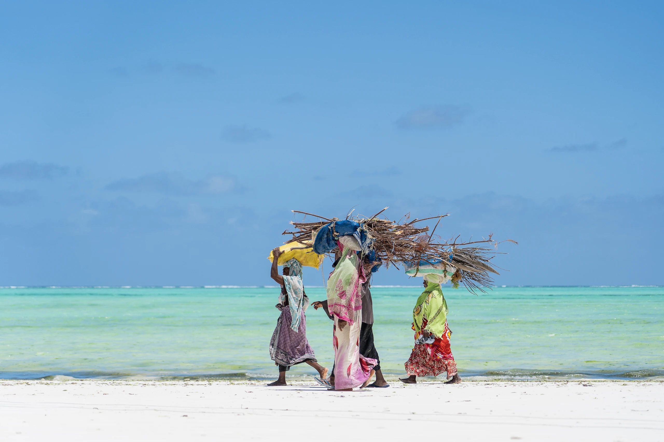 Zanzibari women walking along a turquoise-water beach